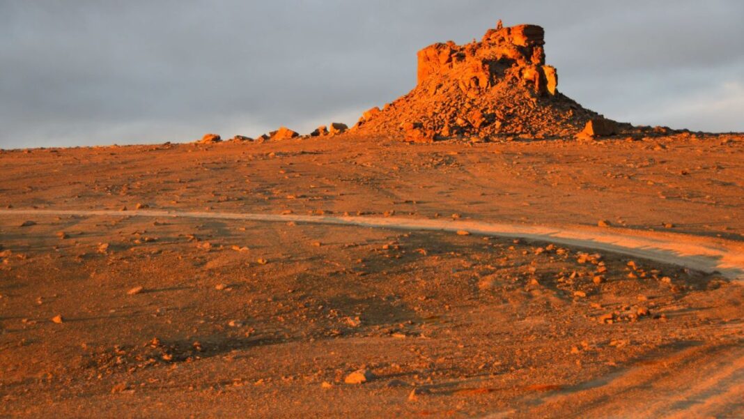 The sun sets on a barren red landscape in the Arctic.