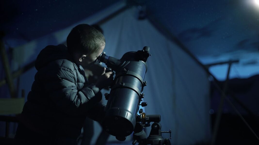 Best telescopes for kids: Image shows young boy using telescope near tents