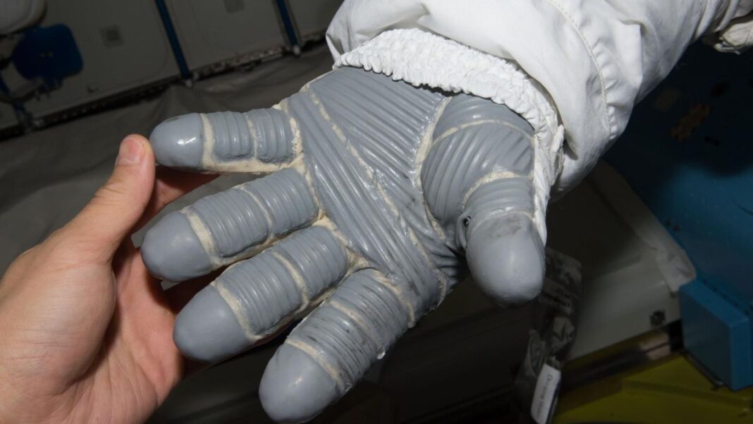a spacesuit glove next to an ungloved hand