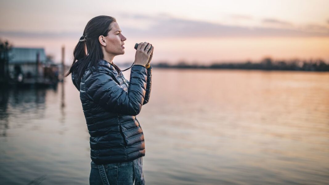 Best compact binoculars: Image shows woman holding binoculars looking out to sea