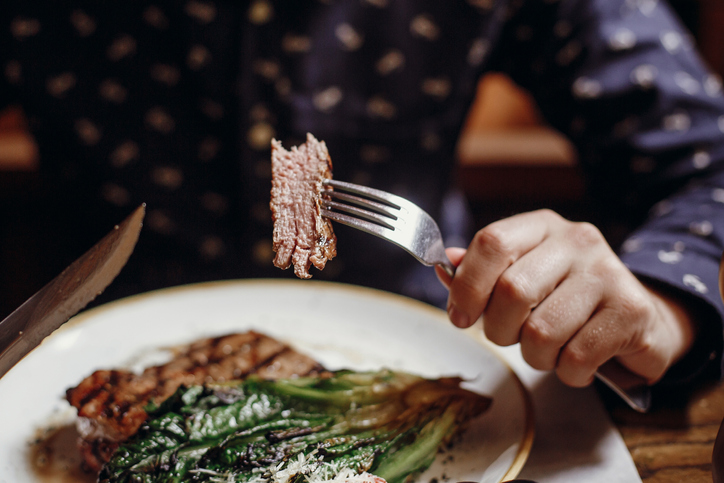 Man holding fork and knife while eating steak