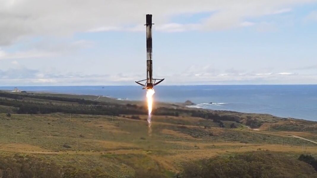 A black-and-white spacex rocket comes down for a landing at a seaside pad with the ocean visible in the background.