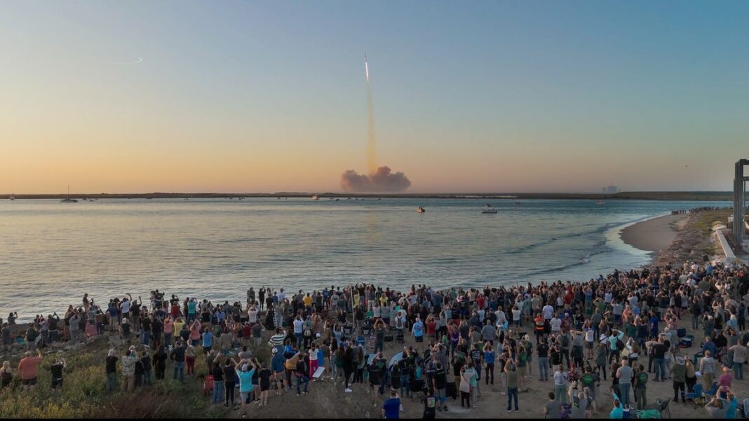 A crowd of people on a beach watches the second-ever test flight of SpaceX